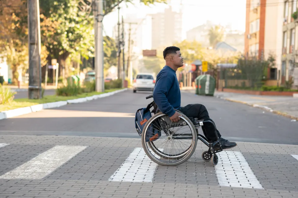 Young man in wheelchair crossing zebra crosswalk.